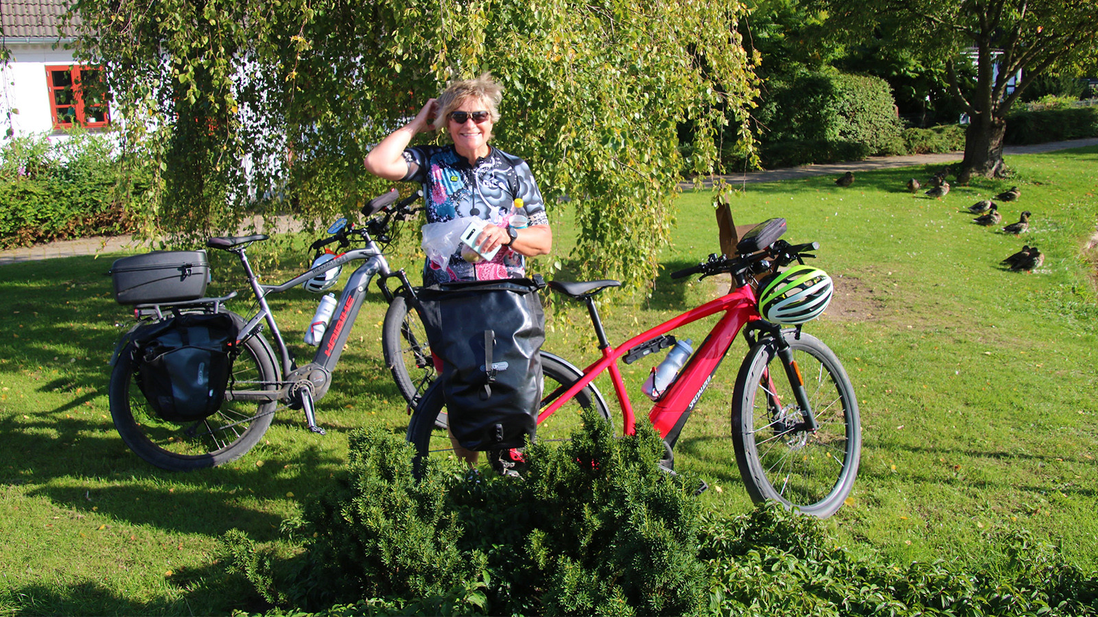 Smilende kvinde i cykeltøj står bag sin cykel i en park