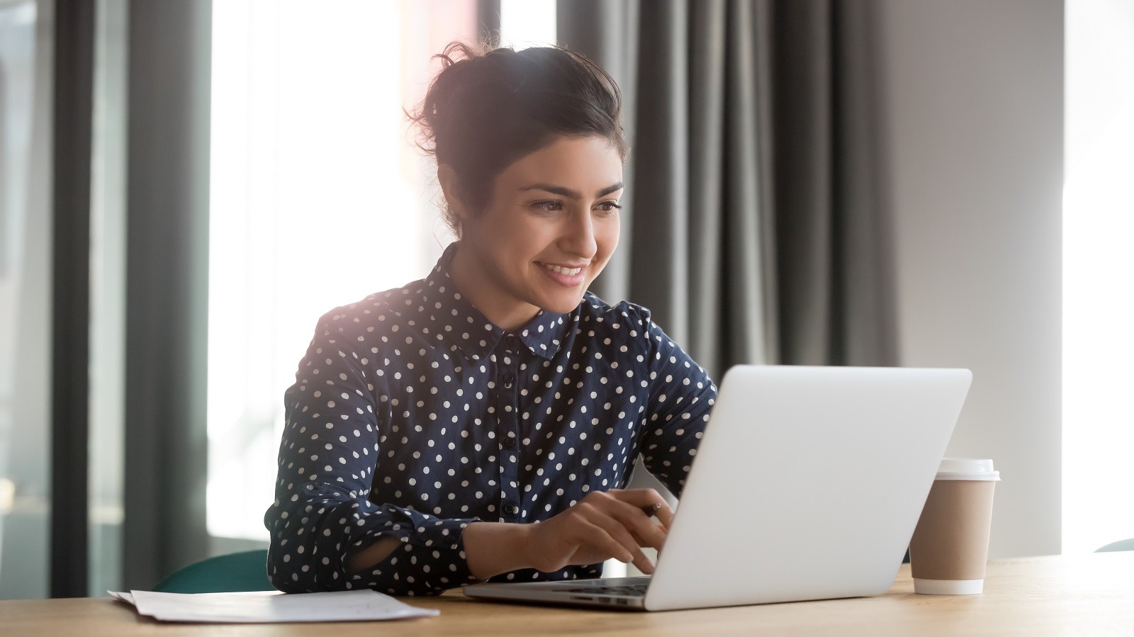 Kvinde i polkaprikket skjorte, der kigger entusiastisk på computerskærm