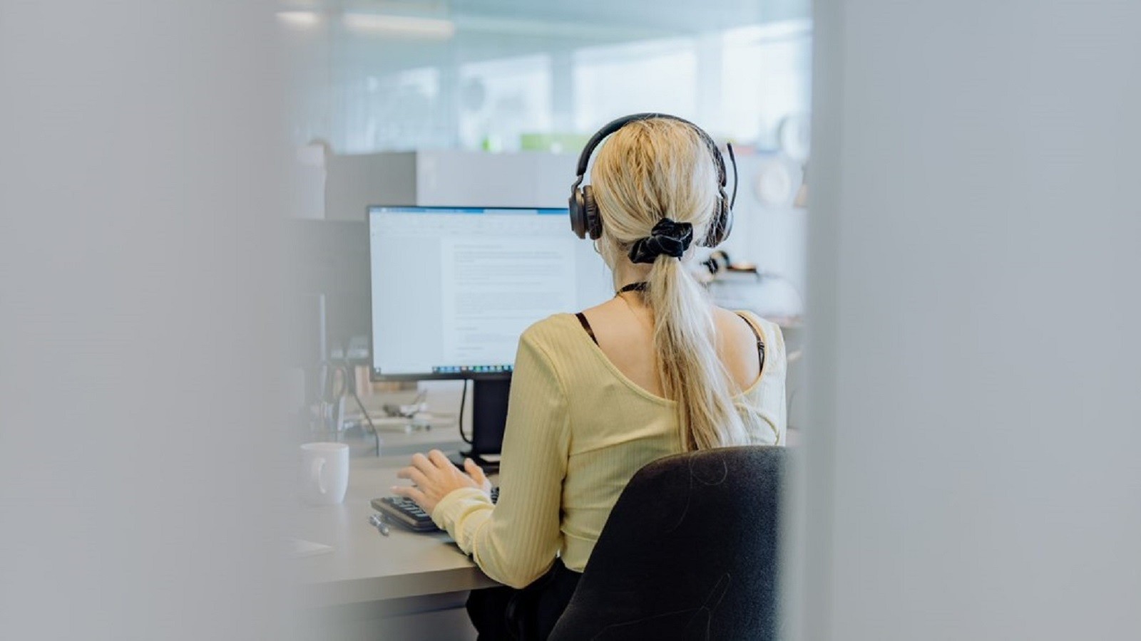 Kvindelig KMD medarbejder, der sidder og arbejder ved sit skrivebord med høretelefoner på set bagfra