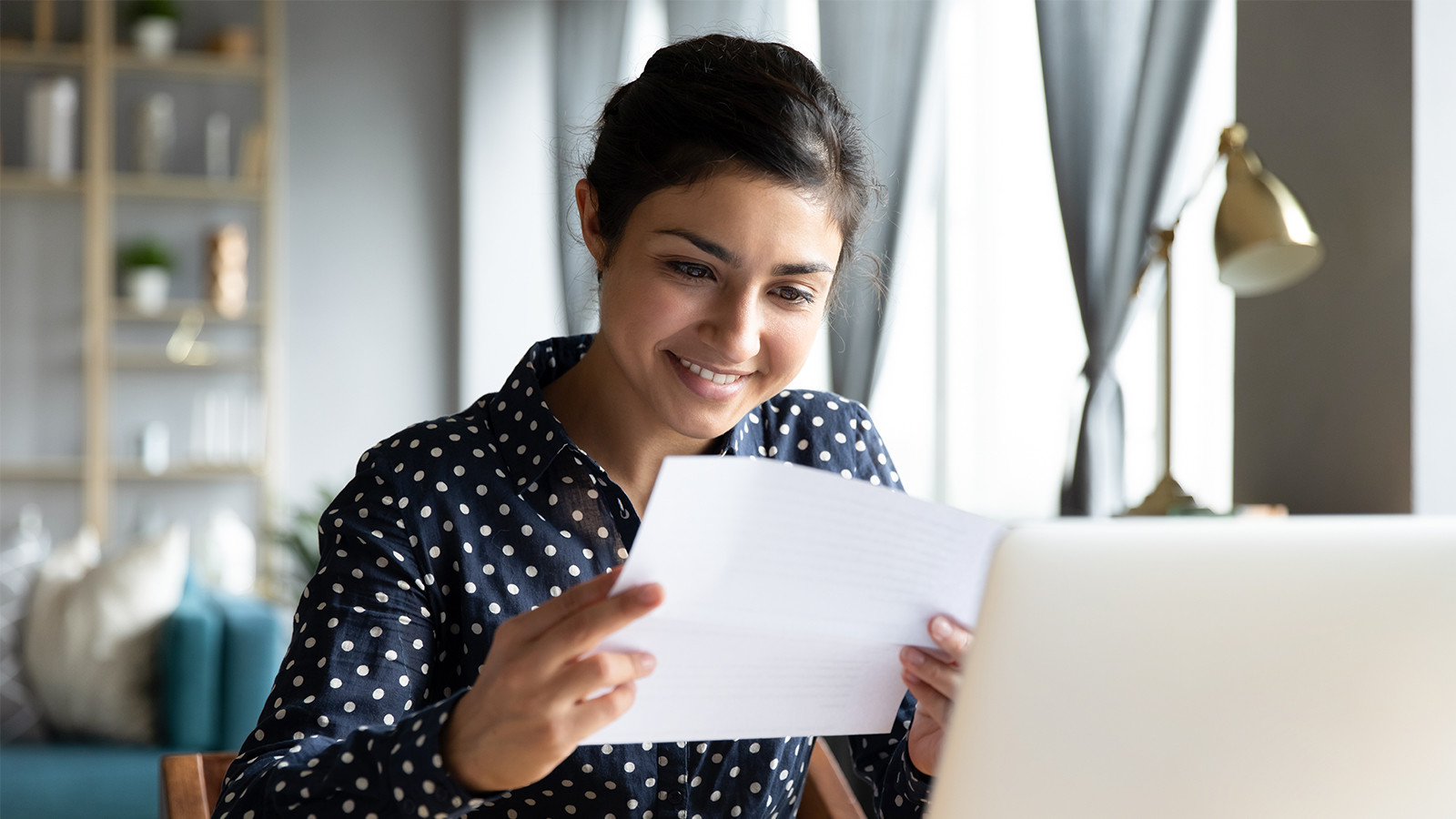Smilende kvinde, der læser et brev foran computeren