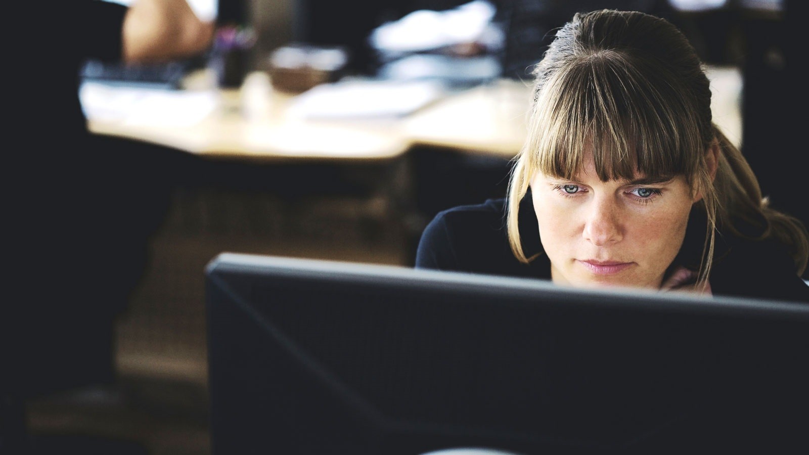 Kvinde kigger koncentreret på computerskærm i kontormiljø