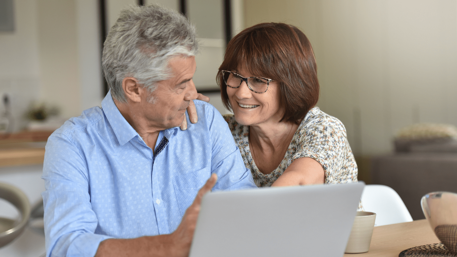 Ældre ægtepar, der smiler til hinanden foran en computer