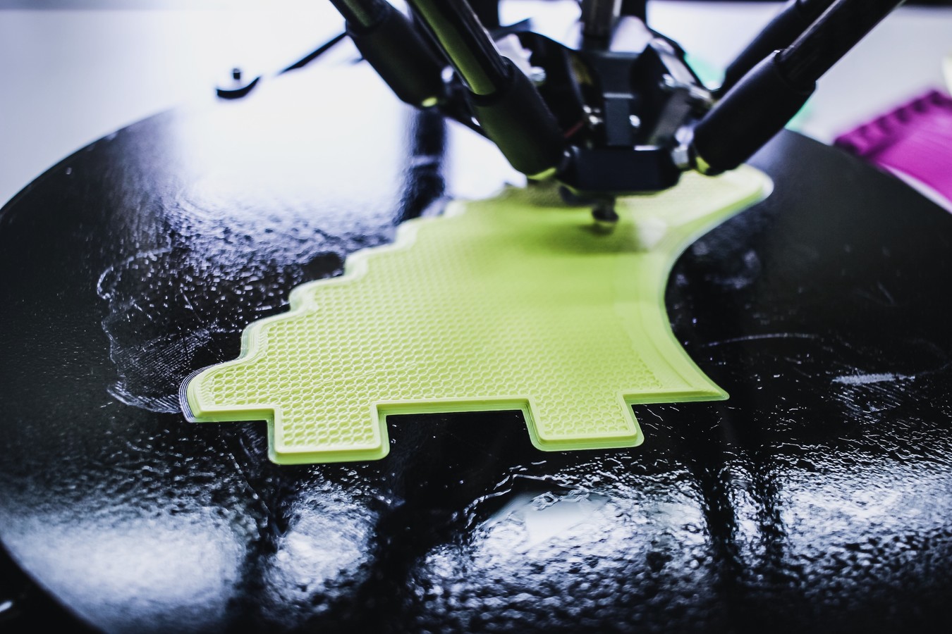 3D-printer, der er ved at printe en grøn figur på en sort flade