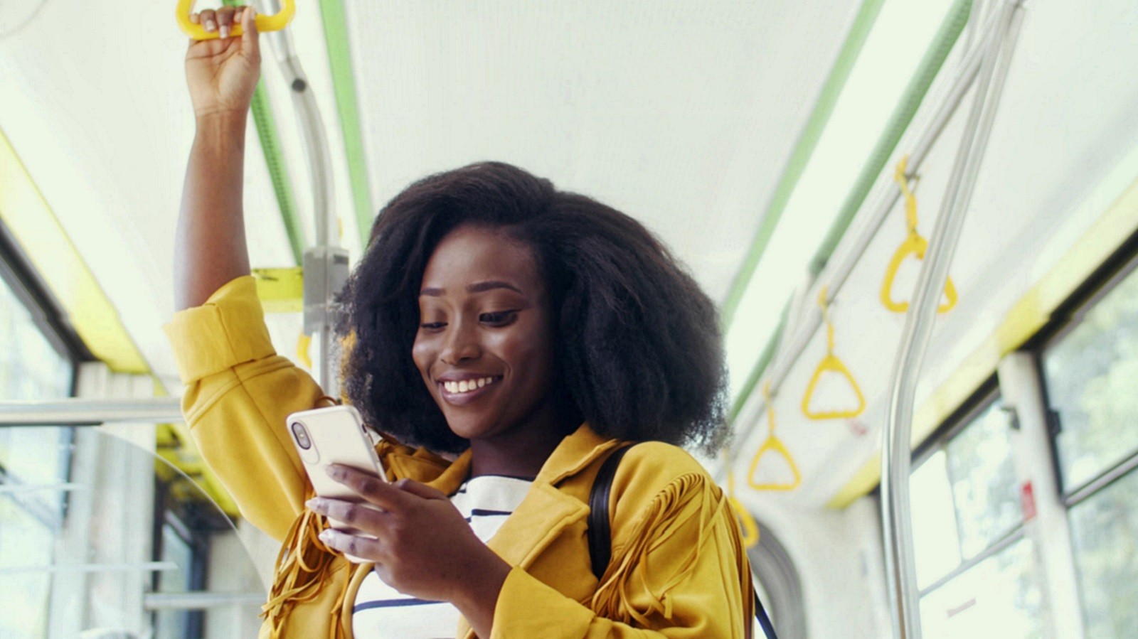 Smilende ung kvinde, der kigger på sin telefon i bussen