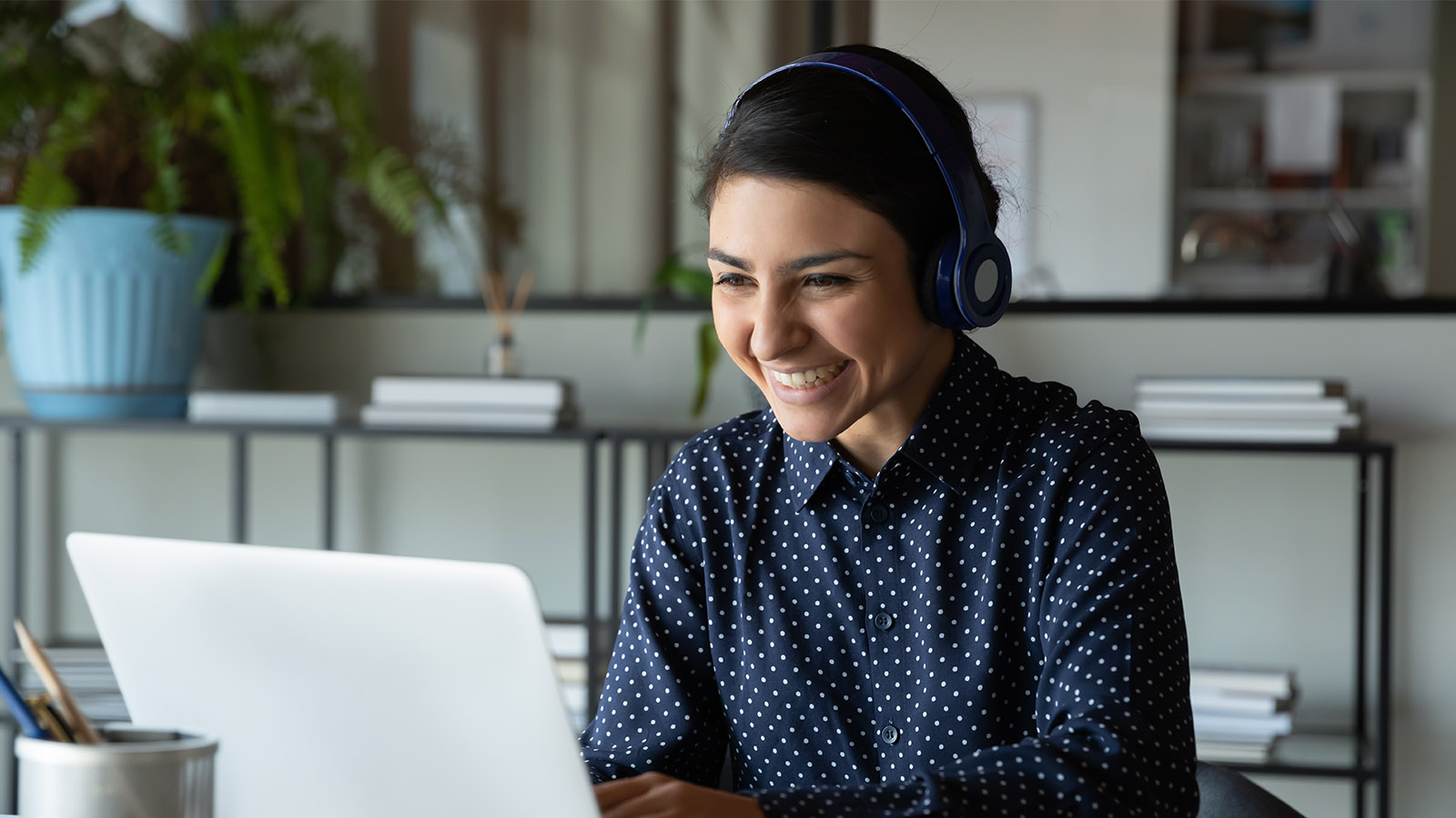 Smilende kvinde med headset på foran sin bærbare computer