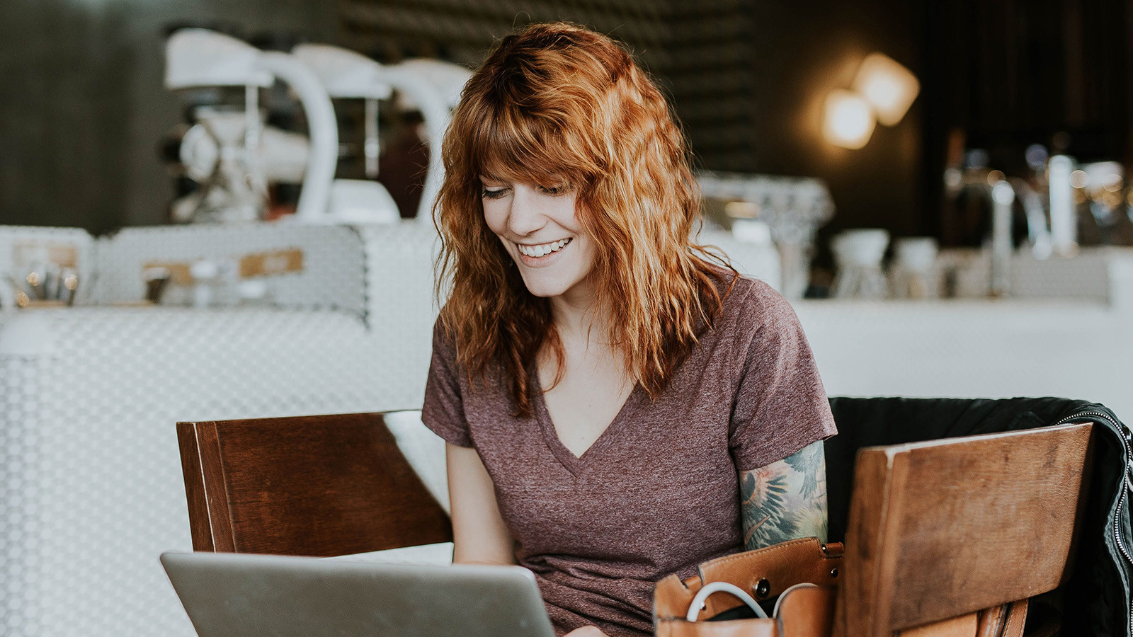 Glad kvinde sidder foran computer og arbejder på en café